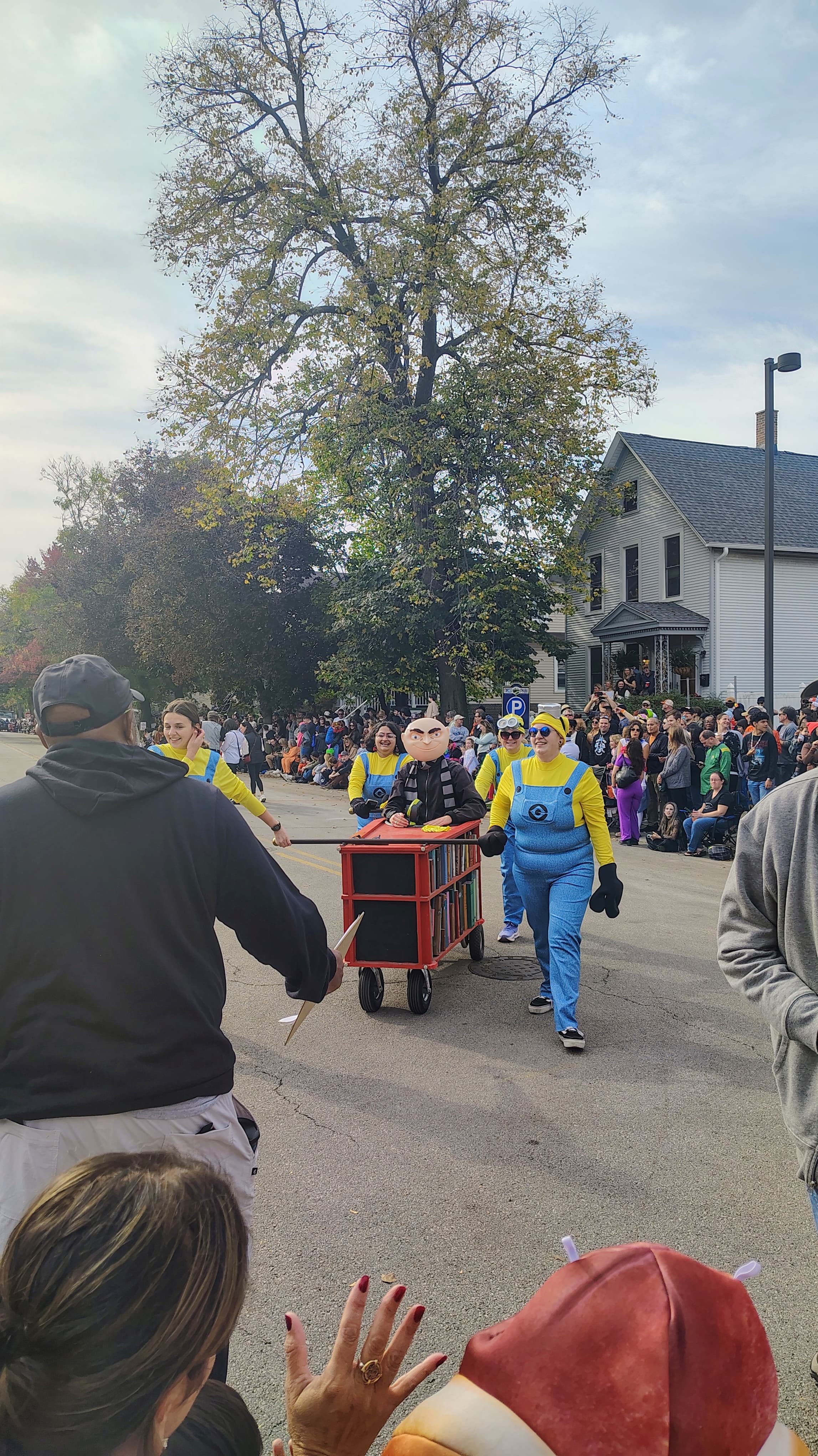 A team in yellow and blue Minion costumes pushing a red bookshelf-shaped casket with a Gru rider waving