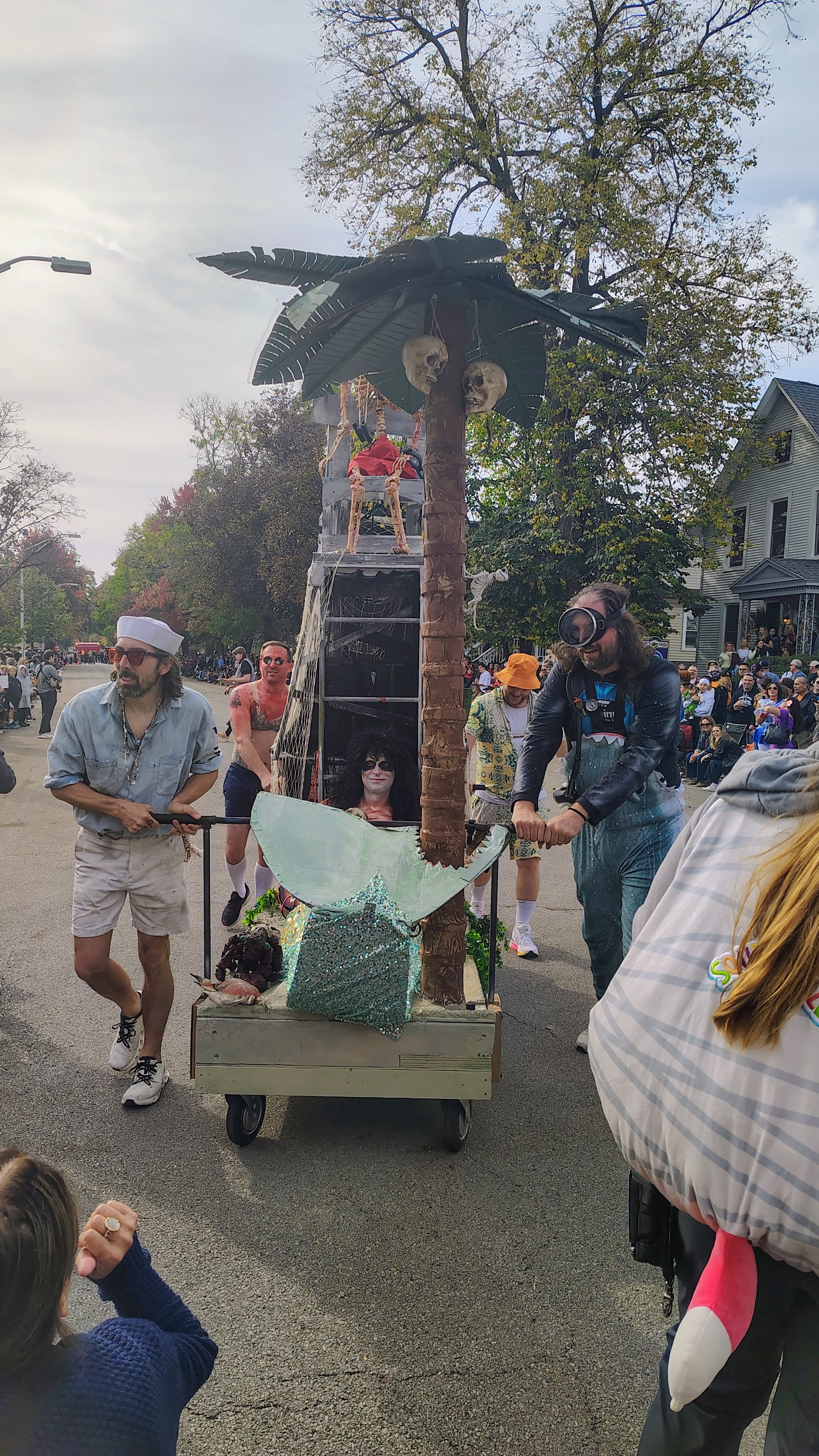 A shipwreck-themed casket with a palm tree, hanging skulls, and a mermaid rider, pushed by a pirate crew