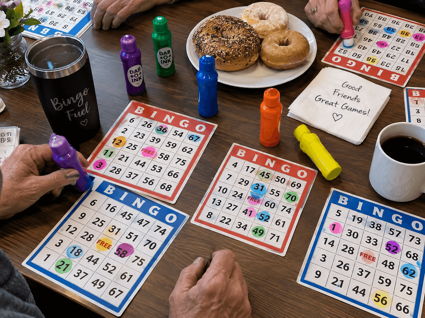 Bingo cards, daubers, and coffee next to a plate of bagels and donuts on a table