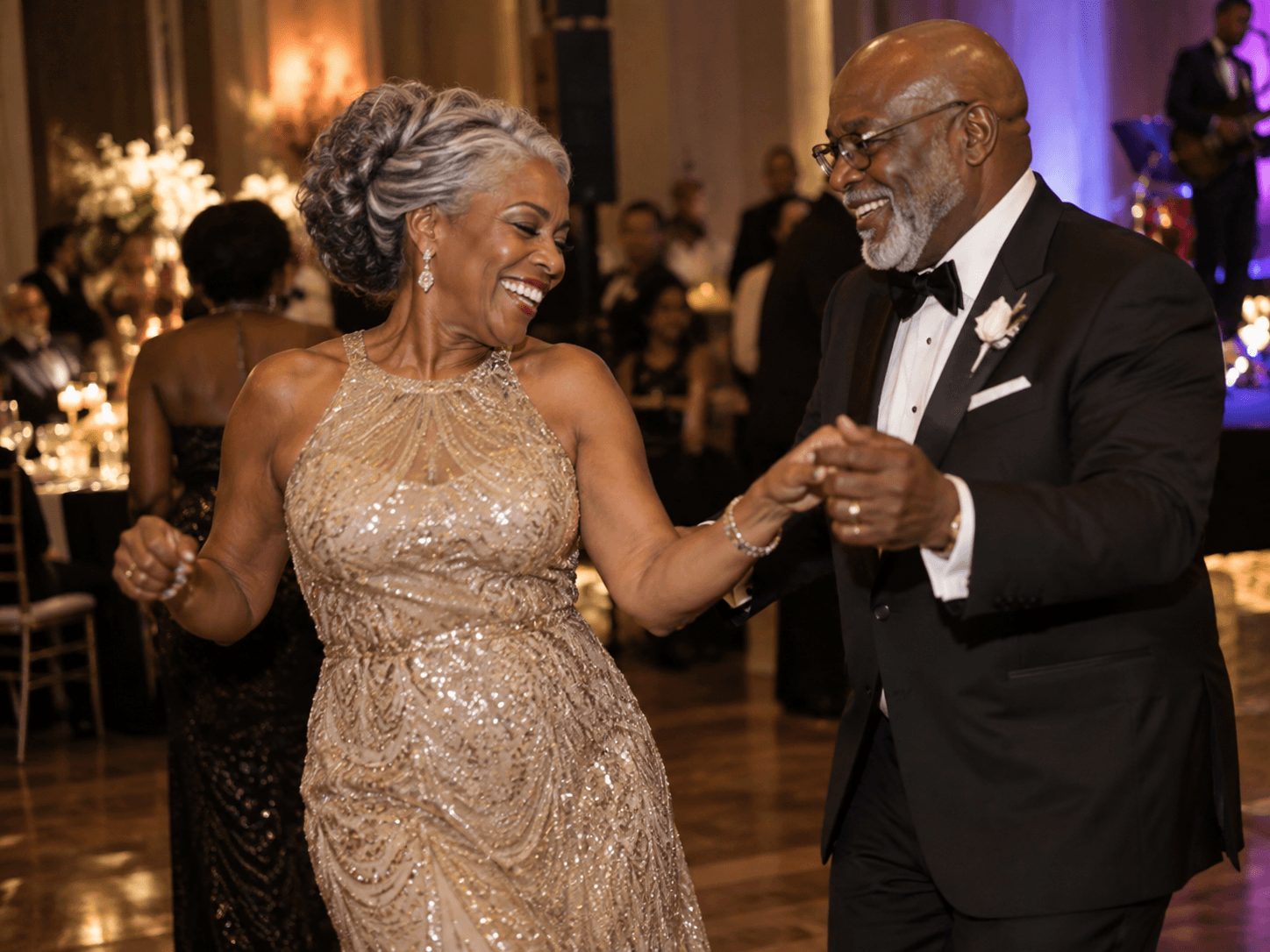 A Black couple in their 60s dancing together at an evening event, both smiling